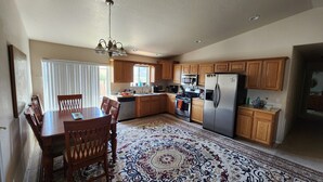 A spacious kitchen with wooden cabinets, a stainless steel refrigerator, and a dining area with a patterned rug.