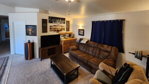 A living room with a ceiling fan, a flat-screen TV, a brown sofa, a coffee table, and a wall-mounted TV stand.