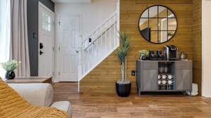 A modern living room with a staircase, a coffee station, and a potted plant.