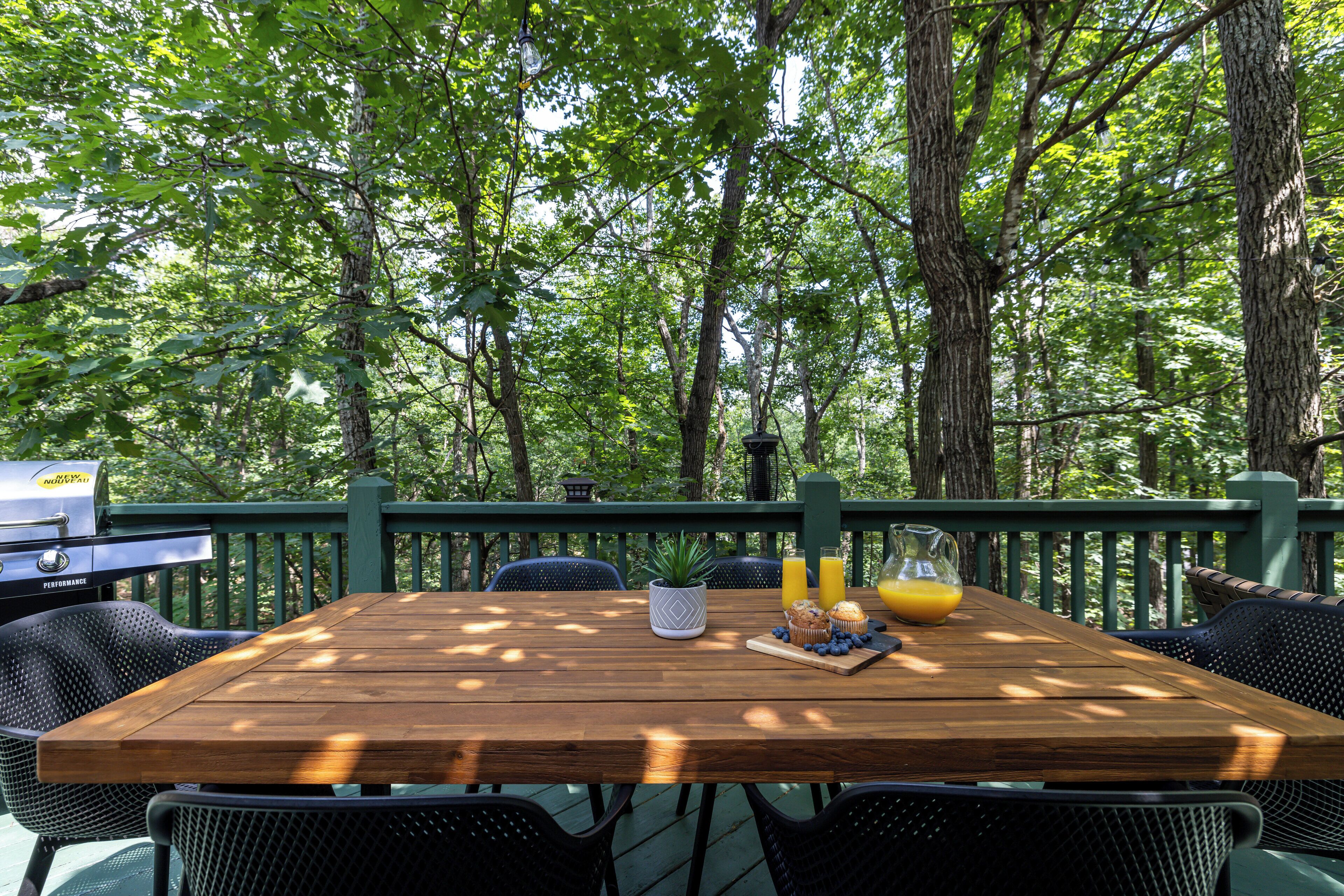 A wooden deck with a table set for breakfast, surrounded by chairs, and overlooking a forested area.
