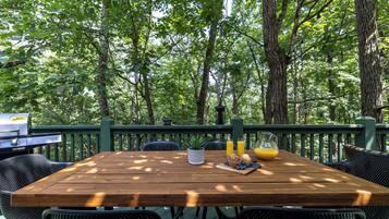 A wooden deck with a table set for breakfast, surrounded by chairs, and overlooking a forested area.