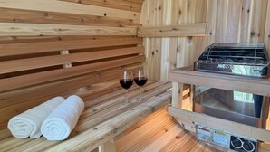A wooden sauna room with two towels, two glasses of red wine, and a sauna heater.
