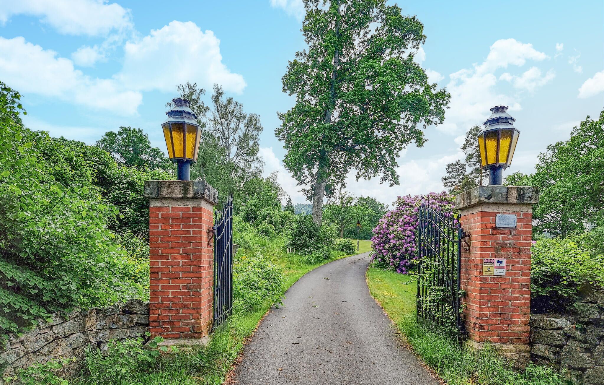 A pathway leading through a brick gate with two street lamps on either side.