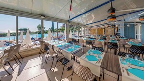 Un restaurant amb terrassa que dona vistes a una piscina i vegetació. Les taules tenen estris amb camises blaves i tovallons blancs.
