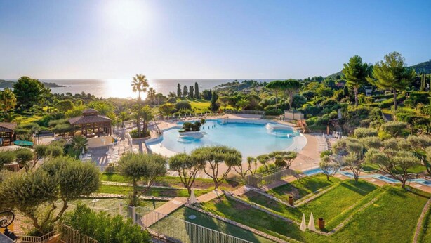 Un complex turístic amb una gran piscina, palmeres i vistes al mar.