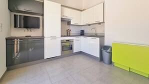 A modern kitchen with white cabinets, a stainless steel range hood, a built-in oven, and a grey trash bin. - Seafront apartment 4 people - 2 Pools (Saint-Raphaël)