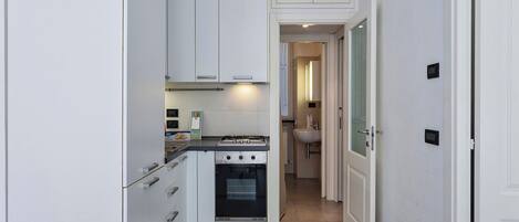 A narrow kitchen with white cabinets, a stove, and a sink.