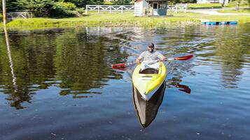 A person in a yellow kayak on a calm body of water with a small dock and a white building in the background.