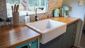 A kitchen with a large sink, wooden countertop, and a view of the outdoors through a window.