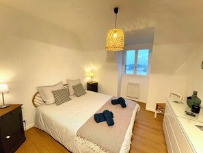 A bedroom with a bed, bedside tables, a lamp, a dresser, and a view of the city through a window.