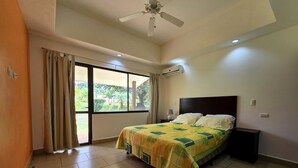 A bedroom with a bed, a ceiling fan, an air conditioning unit, a window with curtains, and a view of greenery outside. - Casa Mandarina Junge Villa 3 pools (Veintisiete de Abril)