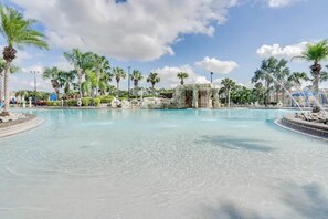 Una gran piscina al aire libre con agua cristalina, rodeada de palmeras y una estructura rocosa.