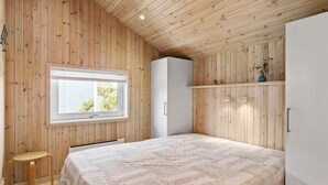 Ein Schlafzimmer mit Holzwandverkleidung, einem großen Bett mit floraler Steppdecke, einem Fenster mit Blick auf B äume und einem weißen Kleiderschrank.