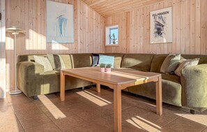 Une pièce chaleureuse au décor intérieur en bois, avec un canapé vert, une table en bois et des œuvres d’art accrochées aux murs.