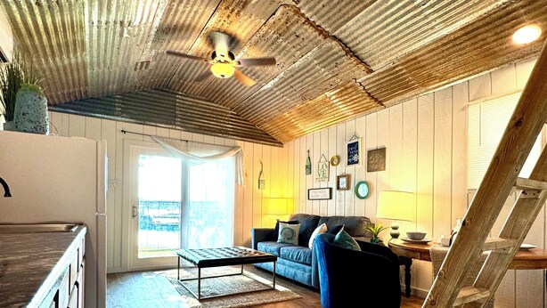 A rustic interior with a wooden ceiling, a sofa, a coffee table, and a ladder.
