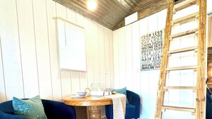 A room with wooden flooring, a wooden table, two blue sofas, a ladder, and a wall with a motivational quote.