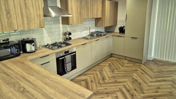 A modern kitchen with wooden cabinets, a stainless steel range hood, a microwave, a coffee maker, and a dishwasher. - Spacious City Living / Free Parking (Birmingham)