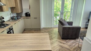 A modern kitchen with a wooden countertop and a bar stool, a grey sofa, and a herringbone-patterned floor. - Spacious City Living / Free Parking (Birmingham)