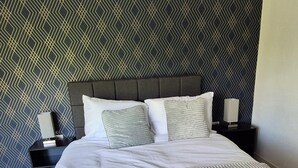 A neatly made bed with a striped blanket, a dark headboard, and a geometric patterned wall. - Spacious City Living / Free Parking (Birmingham)