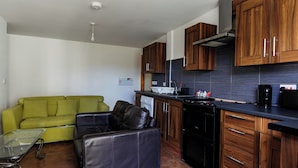 A compact kitchen with wooden cabinets, a black stove, and a green sofa. - The No.10  (Manchester)
