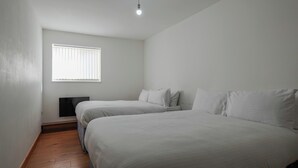 A minimalist bedroom with two beds, a window with blinds, and a wooden floor. - The No.10  (Manchester)