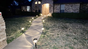 A pathway leading to a stone building with a dark roof, surrounded by grass and a brick wall. - Large 4-bd 3 bath home + bonus room. Dogs are welcome. Sleeps 16+ (Abilene)