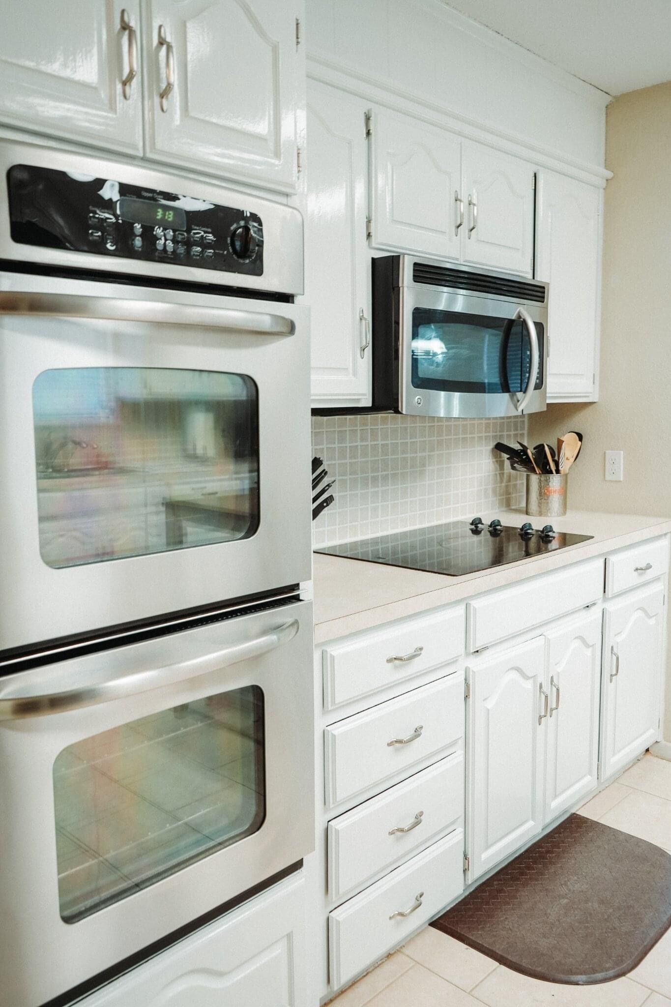 A kitchen with white cabinets, a stainless steel oven, a microwave, and a sink.