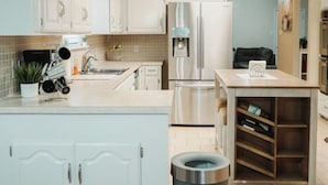 A modern kitchen with white cabinets, stainless steel appliances, a small dining table, and a trash can. - Large 4-bd 3 bath home + bonus room. Dogs are welcome. Sleeps 16+ (Abilene)