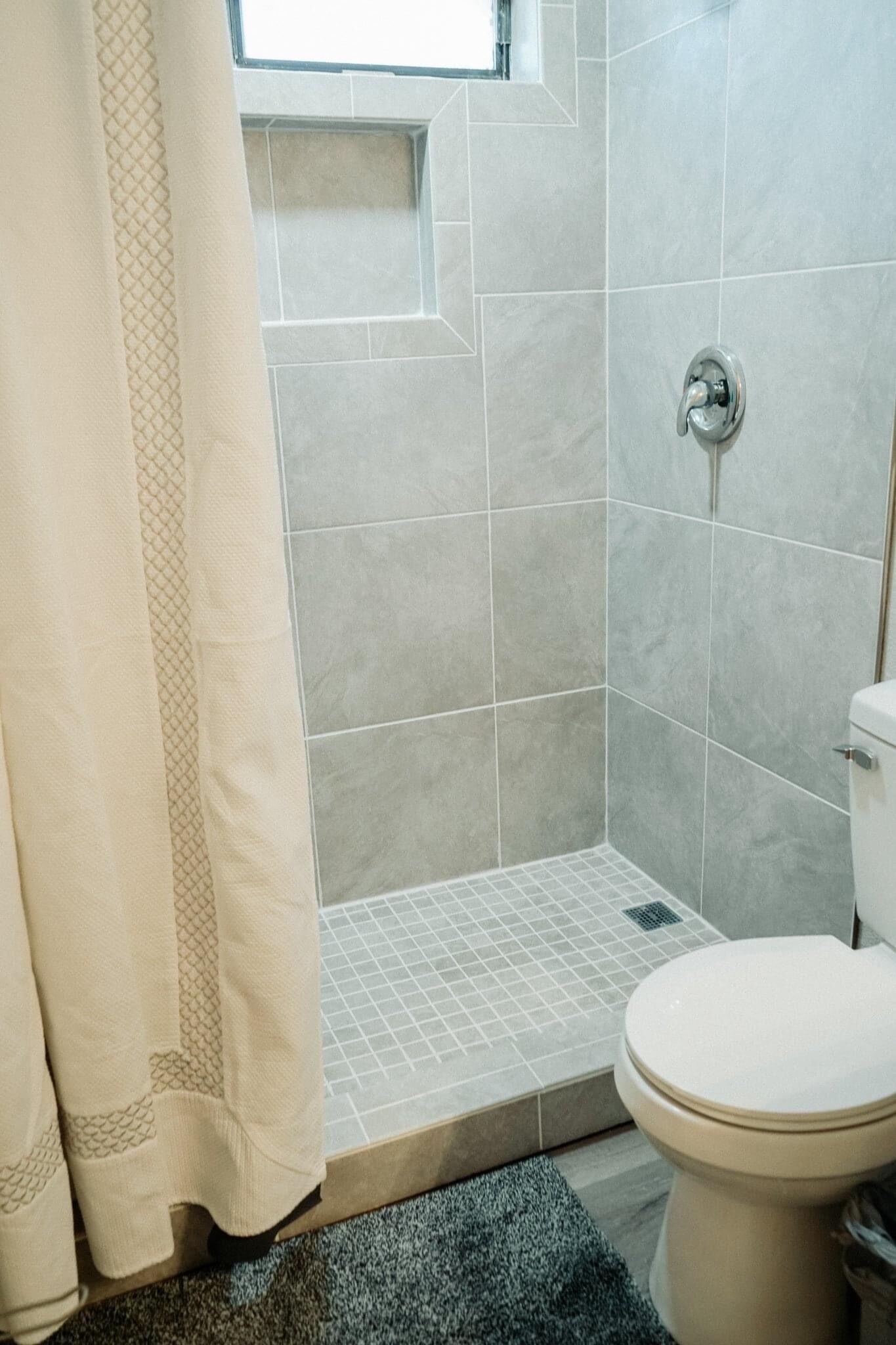 Een badkamer met douche, toilet en een raam.