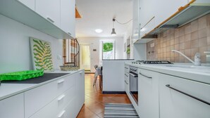 Una cocina estrecha con armarios blancos, una estufa y un área de comedor visible al fondo.