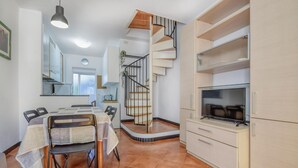Un apartamento moderno con comedor, una escalera en espiral y un televisor sobre un mueble de madera.