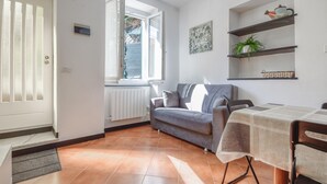 Una sala de estar con un sofá gris, una mesa de comedor con mantel y una ventana que ofrece vistas al exterior.