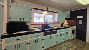Una cocina con gabinetes color turquesa, una encimera negra, una ventana, un fregadero, una estufa y un microondas.