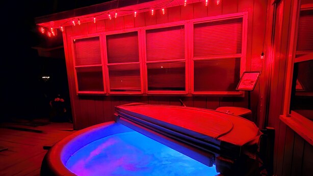 Un jacuzzi con luz azul, rodeado de iluminación ambiental roja y una estructura de madera con contraventanas cerradas.