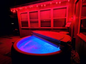 Een hottub met blauw licht, omgeven door rood sfeervol licht en een houten constructie met gesloten luiken.