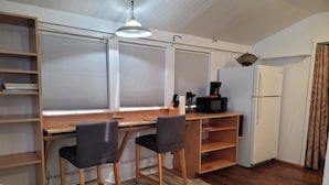 A compact kitchen with a wooden table, two chairs, a white refrigerator, and a coffee maker.