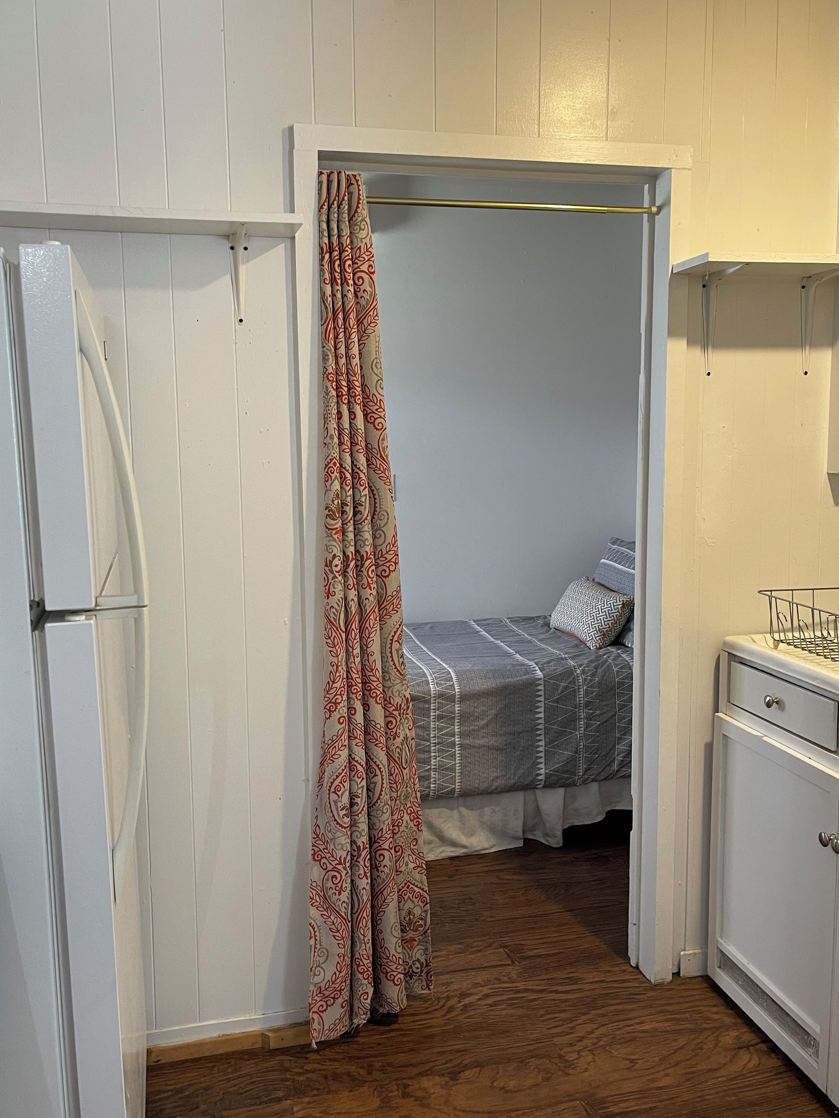A small bedroom with a bed, a wardrobe, and a curtain.