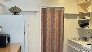 A compact kitchen with white cabinets, a microwave, a stove, and a wooden dining table.