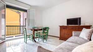 Een woonkamer met een bank, een eettafel met stoelen, een televisie op een houten kast en een schuifpui die leidt naar een buitenruimte.