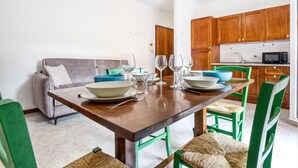 Een eetruimte met een houten tafel gedekt voor vier personen, omringd door groene stoelen met geweven zittingen.