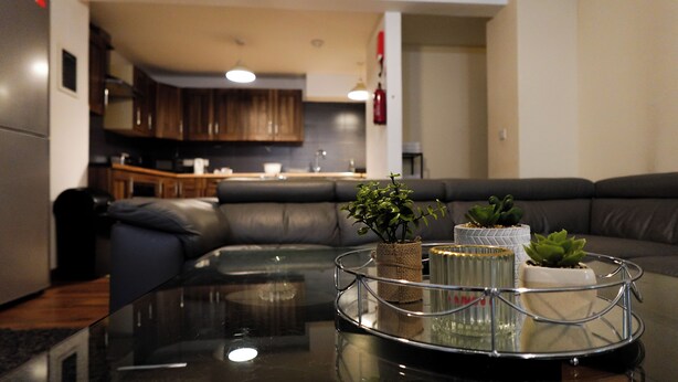 A modern living room with a glass coffee table, leather sofa, and potted plants. - The Blissful Heaven (Manchester)