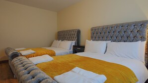A hotel room with two beds, a bench, and a nightstand. - The Blissful Heaven (Manchester)
