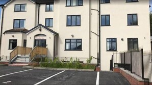 A multi-story building with a flat facade, a front entrance with steps, and a parking area in front. - The Blissful Heaven (Manchester)