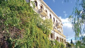Un bâtiment historique doté de nombreux balcons et d’arcades, entouré d’une végétation luxuriante.