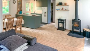 A modern kitchen with a central island, a dining area with wooden chairs, a cozy living room with a sofa, and a wood-burning stove. - Amazing home in Ebeltoft with WiFi (Ebeltoft)