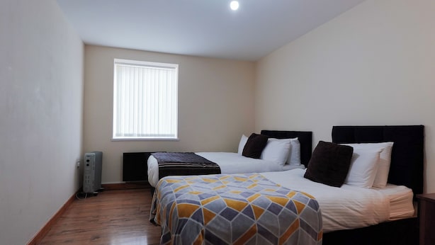 Une chambre avec deux lits, une fenêtre avec des stores, un radiateur et un plancher en bois.