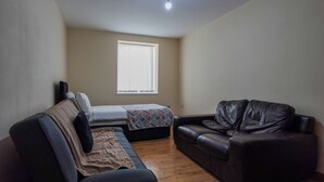 Une petite pièce meublée, comprenant un lit, un canapé et un fauteuil en cuir.
