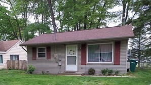 A single-story house with a front porch, a small front yard, and a neighboring house. - Family Friendly Lake View Home. Only steps away from Houghton Lake. (Houghton Lake)