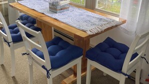 A dining area with a wooden table, white chairs with blue cushions, and a lace table runner. - Family Friendly Lake View Home. Only steps away from Houghton Lake. (Houghton Lake)