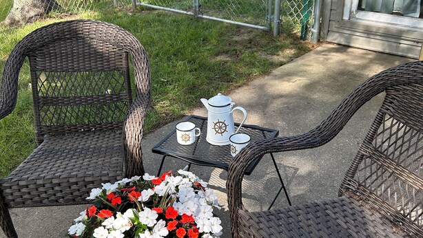 A patio with wicker chairs, a small table, and a potted plant with flowers. - Family Friendly Lake View Home. Only steps away from Houghton Lake. (Houghton Lake)